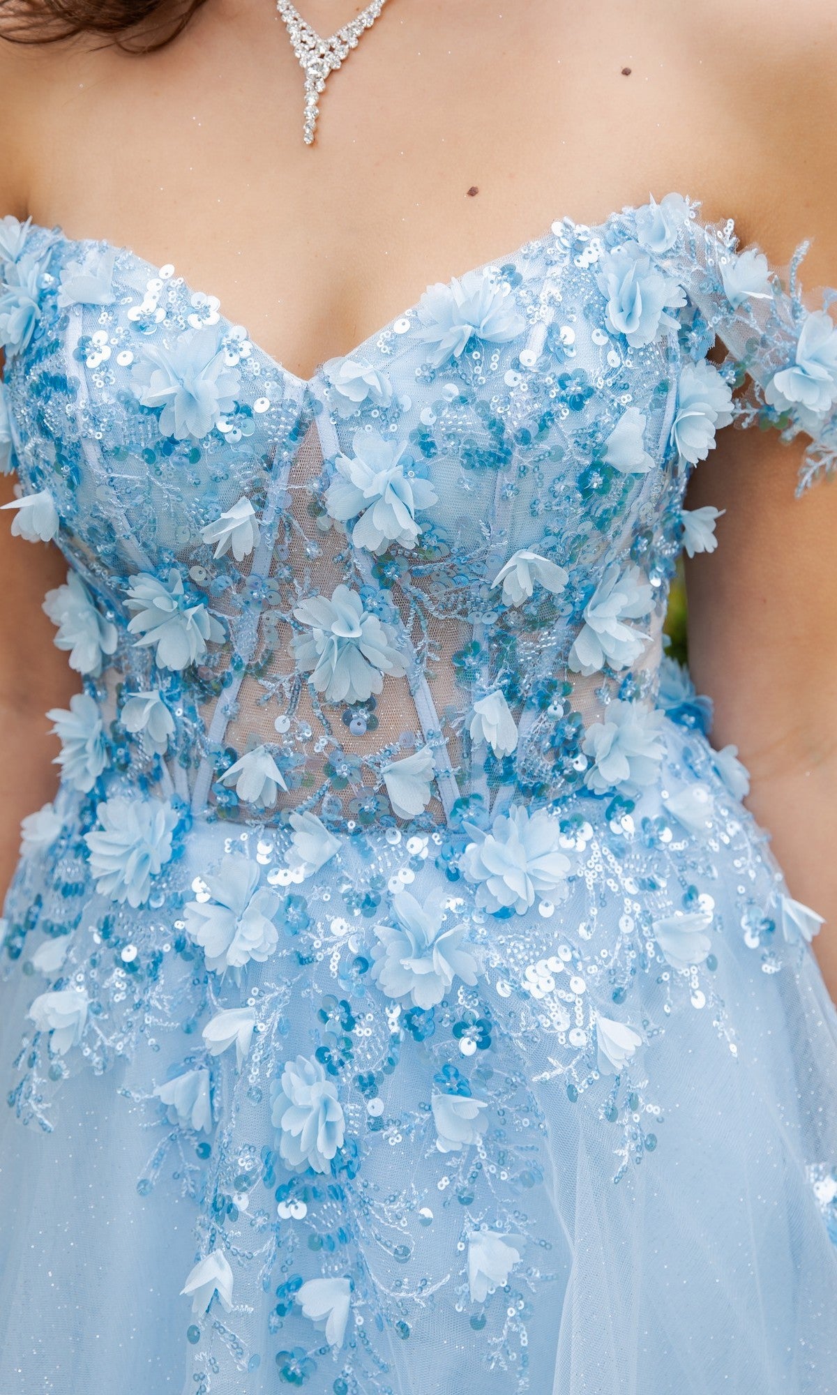 Close-up of a person wearing the Cinderella Couture 8403J long prom dress, a strapless light blue gown adorned with 3D floral appliqués, sequins, beadwork, and paired with a silver necklace.